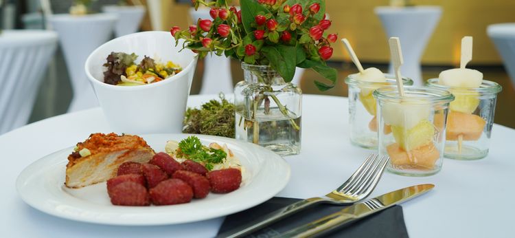 Gedeckter Tisch mit Speisen auf Teller, daneben Salatschale und Nachtischgläser mit Obst