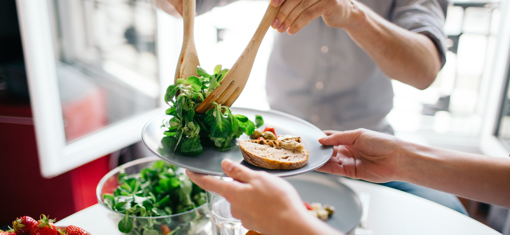 Person gibt Feldsalat auf einen Teller auf dem eine Scheibe Baguette liegt
